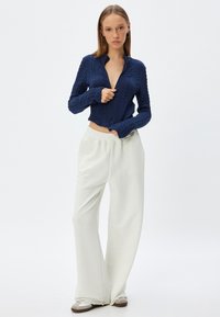 Marinblå stickad kort tröja med kabelstickad design, som har en djup V-ringning. Kombinerad med löst sittande krämfärgade byxor och sneakers.