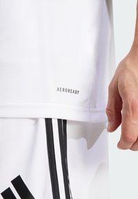 White athletic shirt with Aeroready branding, smooth texture, and short sleeves; paired with shorts featuring black accent stripes.