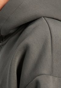 Gros plan sur une personne portant un sweat à capuche gris foncé, mettant l'accent sur la texture du tissu de l'épaule et les détails de couture de la capuche.