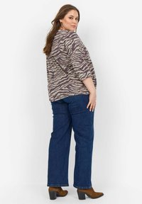 T-shirt con motivo a righe zebrate in tonalità di beige e viola scuro, abbinato a jeans dritti blu scuro e stivaletti alla caviglia marroni con tacco.