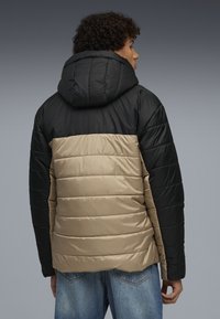 Polstret jakke med sort hætte og ærmer, beige krop og lodrette syninger. Har en glat overflade og en regular fit.