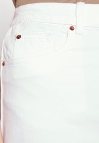 I pantaloni corti in denim bianco presentano una tasca frontale, accessori in tonalità rame e una texture sottile. La cintura è cucita per garantire durata.