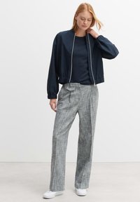 Marine bomberjack met een ritssluiting aan de voorkant en elastische manchetten, gecombineerd met lichtgrijze geruite broek met een strikdetail op de tailleband.