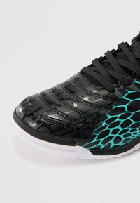 Pantofel sport negru cu un superior texturat ce prezintă un model de crocodil. Accente aqua pe laterale, vârf rotunjit și talpă albă.