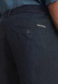 Navy blue linen trousers with a smooth texture, featuring a single back pocket and a button closure; includes a small brand label.