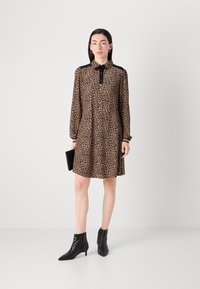 Leopardenmusterkleid mit Kragen, langen Ärmeln und schwarzen Akzenten. Getragen mit knöchellangen schwarzen Stiefeletten und einer schwarzen Clutch.