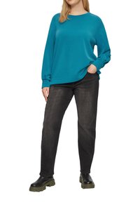 Tannengrüner Langarm-Sweatshirt mit runder Ausschnitt, kombiniert mit dunkelgrauen, lässig sitzenden Jeans und schwarzen, klobigen Stiefeln. Glatte Stofftextur.