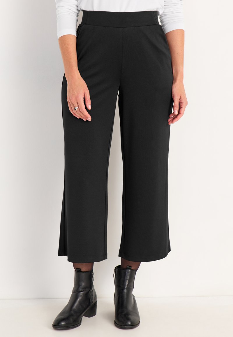Zwarte, wijde broek met een gladde textuur, hoge tailleband en zijsplitten; gecombineerd met zwarte enkellaarzen.