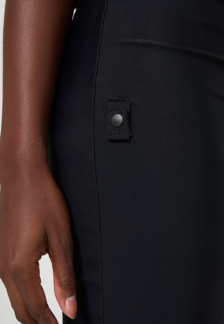 Schwarze Leggings verfügen über ein strukturiertes Panel mit einem Druckknopfverschluss an der Seite, das einen glatten, dehnbaren Stoff und eine maßgeschneiderte Passform betont.