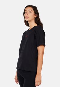 Černé tričko s krátkým rukávem vyrobené z bavlny, s kulatým výstřihem a malým červeným logem na prsou. Hladká textura, volný střih.