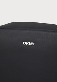 Black faux leather bag with smooth texture. Features a silver "DKNY" logo on the front, simple design with minimalist details.