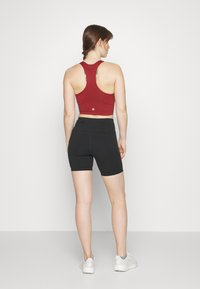 Piros, bordázott sportmelltartó racerback kialakítással; magas derekú fekete sorttal párosítva, amely varrásokkal és sima textúrával rendelkezik.