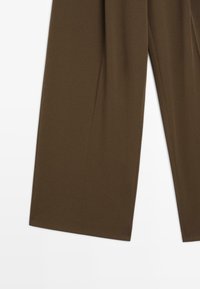 Pantaloni ampi marroni realizzati in tessuto morbido, con una superficie liscia e senza texture e una finitura pulita e sartoriale.