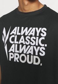 Černé bavlněné tričko s výrazným bílým textem: "VŽDY KLASICKÉ. VŽDY HRDÉ." s dynamickými styly písma a tvary. Kolo výstřih.
