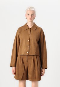 Bruine faux suède cropped jacket met een klassieke kraag, sluiting met knopen aan de voorkant en brede mouwen, gecombineerd met bijpassende geplooide shorts.