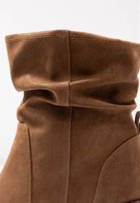 Bottine en cuir marron avec un design décontracté, surface texturée, coutures décoratives et un accent latéral pour le style.