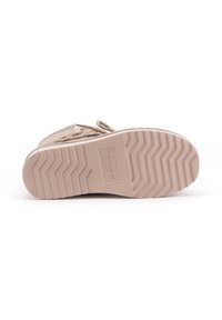 Beige schoeisel met een gestructureerde rubberen zool met een zigzagpatroon en een label dat op de onderkant is gedrukt. Veters zichtbaar op de bovenkant.