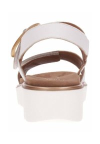 White sandal with a flat sole and brown insole, featuring a wide strap design and a gold accent detail on the side.