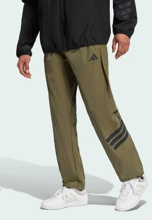 Gröna lätta byxor med en strukturerad yta, med svarta tre-randiga detaljer och en Adidas-logotyp, i kombination med vita sneakers.