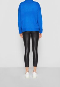 Niebieski, dzianinowy, oversize sweter, czarne, błyszczące legginsy oraz białe buty na platformie, widok z tyłu, podkreślający kontrasty kolorystyczne i teksturalne.