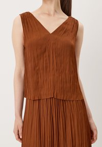 Brown pleated sleeveless top featuring a V-neckline, with a loose fit and textured surface, paired with a coordinating pleated skirt.