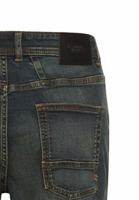 Jeans dżinsowe w ciemnoniebieskim odcieniu z delikatnym przetarciem, z brązową skórzaną naszywką na pasku i standardowymi tylnymi kieszeniami.
