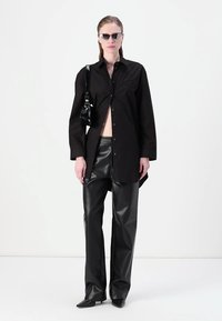 Black button-up shirt with a slit, paired with high-waisted black leather trousers. Accessories include black sunglasses and a small bag.