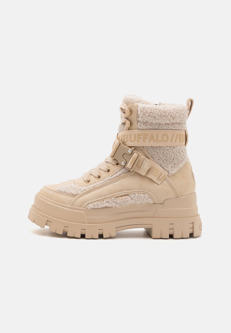Bottines beige à cheville avec un dessus en tissu pelucheux, une semelle en caoutchouc robuste et une sangle à boucle avec accent de marque. Design texturé et élégant.