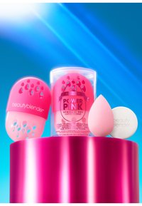 Zestaw startowy Beautyblender Power Pink, zawierający różowy gąbkę, mydło i silikonowe etui z wycięciami w kształcie łezki, wyeksponowany na błyszczącym różowym piedestale.