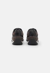 Zapatillas de ante marrón y cuero negro, con un talón texturizado, suela de goma y un detalle de logo minimalista en la parte trasera.