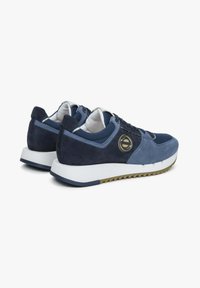 Navy modré sportovní boty s svrchní částí z veluru a síťoviny, bílou mezipodešví, strukturovanou hnědou podrážkou a kruhovým logem na boku.