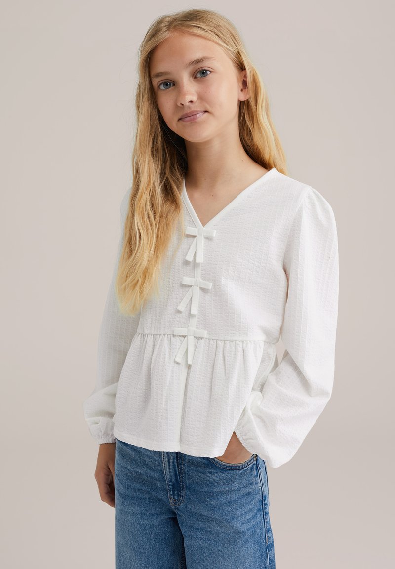 Vit texturerad blus med V-ringning, med knapppynt, långa puffärmar och empireliv. Matchas med blåjeans.