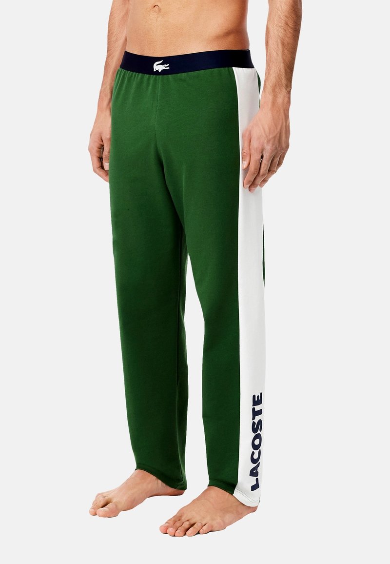 Zöld melegítőnadrág sötétkék derékkal, fehér oldalsávval és kék "LACOSTE" felirattal. Puha, texturált anyagból készült.