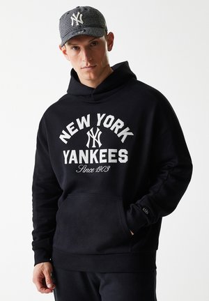Crna kapuljača s grafikom "NEW YORK YANKEES" u bijeloj boji, s prednjim džepom i rebrastim rukavima. Siva kapa s logotipom i uzorkom houndstooth.