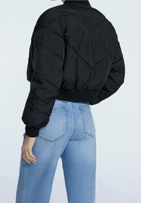 Zwarte donsjack met een doorgestikt ontwerp, geribbelde manchetten en zoom, gecombineerd met lichtblauwe spijkerbroeken. De stof heeft een gestructureerde afwerking.