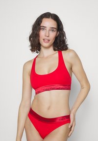 Rød bomulls-bralette med brede stropper og Calvin Klein-logo på elastikkanten; matching rød bikini-stil bunn med lignende logo-detalj.