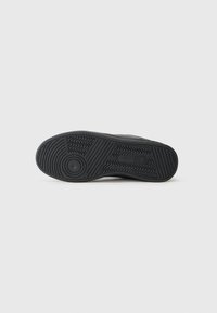 Semelle en caoutchouc noir de basket avec un motif de traction. Comprend un talon circulaire et des éléments de design ondulés pour une prise et une stabilité optimales.