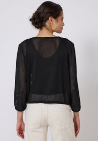 Czarny, przezroczysty top z siateczki o luźnym kroju, dekolcie w serek i rękawach o długości trzy czwarte, z teksturowanym wzorem w kratkę i skróconym dołem.
