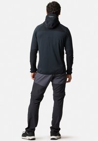 Zwarte lange mouw top met een capuchon en contrasterende donkergrijze broek, met een mix van texturen en ritszakken voor functionaliteit.