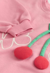 Pink sweatshirt featuring ribbed cuffs, large white graphic, and three-dimensional red cherry applique with green stems. Soft texture.
