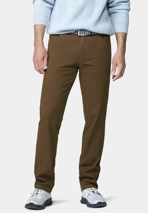 Mann trägt braune Freizeithose, weiße Sneakers, einen hellblauen Pullover und einen gemusterten Gürtel, steht vor einem schlichten Hintergrund.