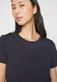 Granatowy t-shirt z krótkim rękawem, okrągłym dekoltem, wykonany z gładkiego materiału, z subtelną fakturą i dopasowanym krojem.