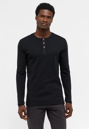 Sort langærmet henley skjorte med rund hals, tre træknapper og et lille logo på venstre bryst, fremstillet af ribbet stof.