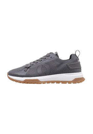 Zapatilla deportiva gris con parte superior de malla texturizada, plantilla blanca y suela de goma marrón. Presenta un logotipo circular y un talón reforzado.
