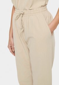 Beige, lightweight pants with an elastic waistband and drawstring. Features side pockets and a textured fabric. Relaxed fit.