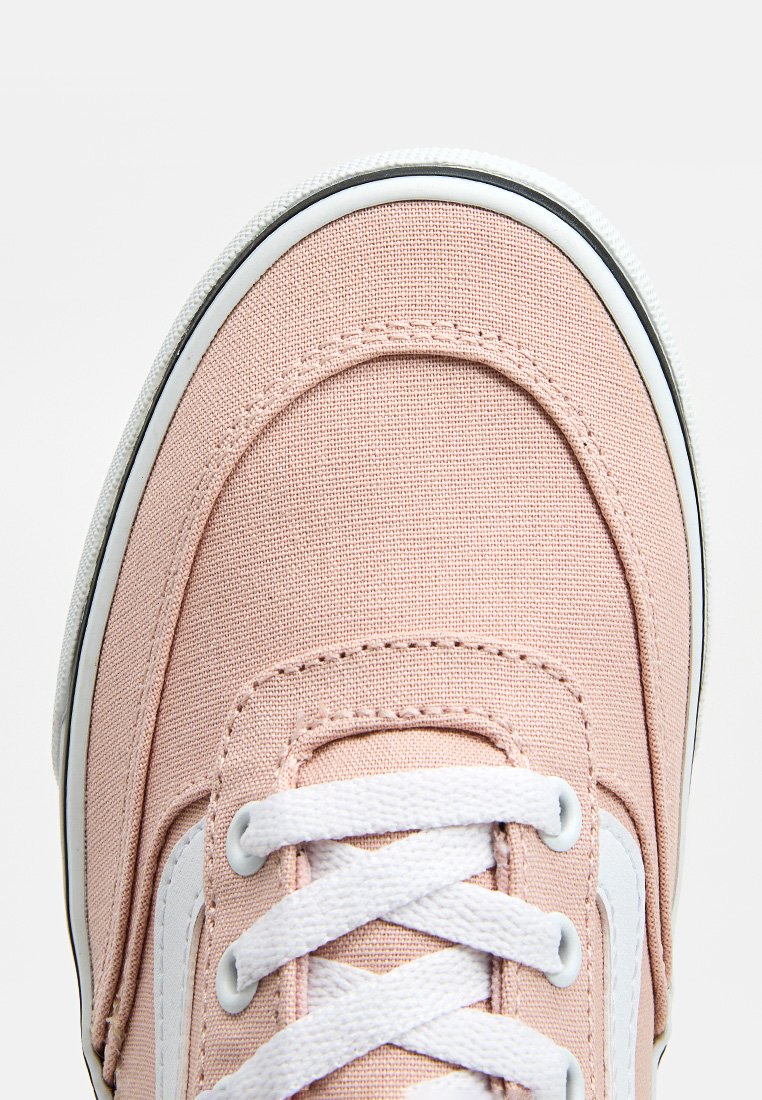 Zapatilla de lona rosa claro con cordones blancos, suela de goma y un acento lateral blanco en contraste. Punta redonda y detalle de tela texturizada.
