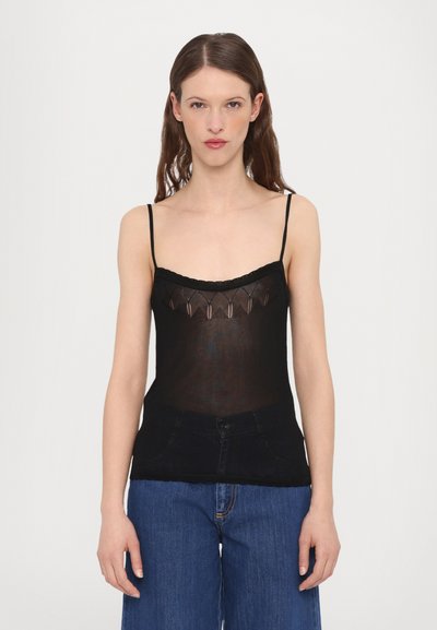 Débardeur noir transparent avec des fines bretelles, ornée d'une finition en dentelle et d'un motif géométrique au niveau de l'encolure, associé à un jean en denim foncé taille haute.