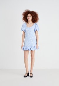 Light blue floral-patterned mini dress with puff sleeves and ruffled hem. Worn with black Mary Jane shoes. Smooth fabric texture.