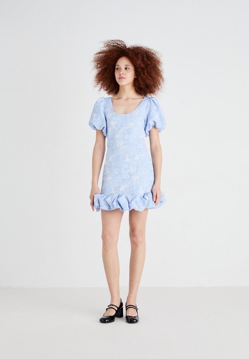 Light blue floral-patterned mini dress with puff sleeves and ruffled hem. Worn with black Mary Jane shoes. Smooth fabric texture.