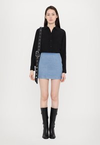 Black button-up shirt with pleated accents, light blue denim mini skirt, and knee-high black leather boots, paired with a decorative belt strap.